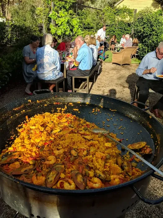 Guests gathered around a paella pan at a backyard celebration